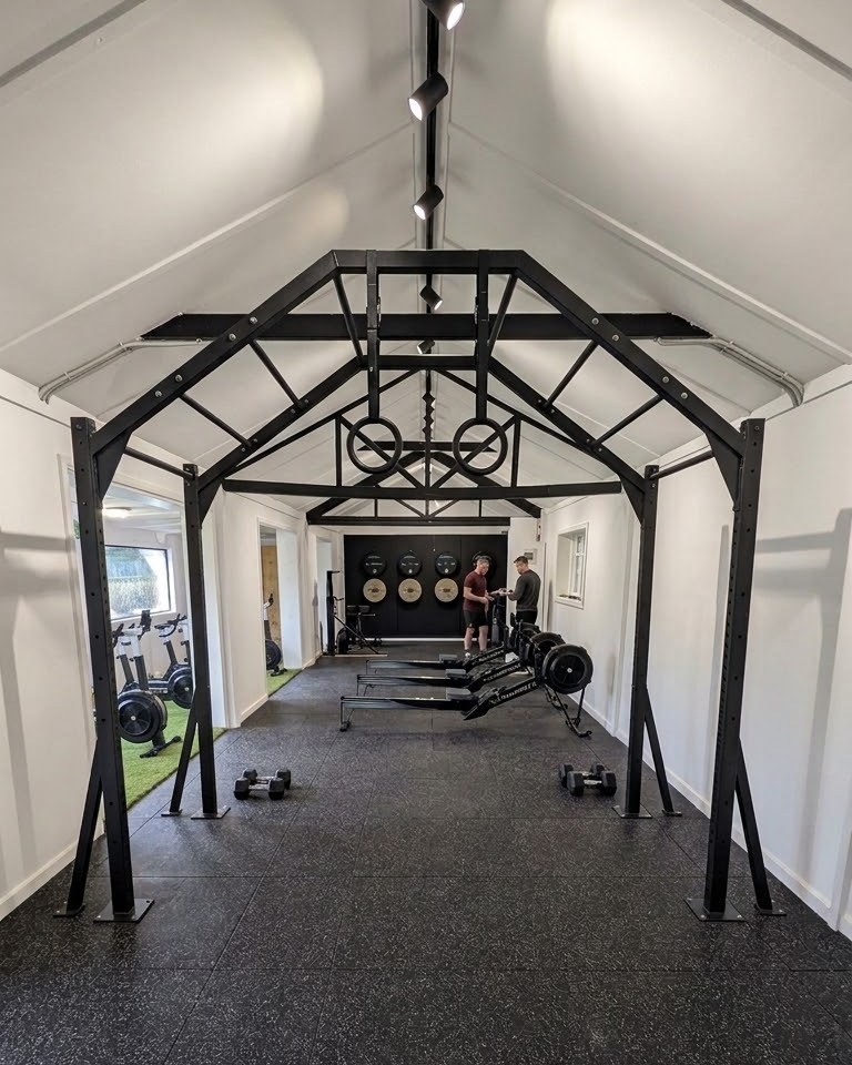 The indoor training studio, with steel roof trusses, rowers and a rubber floor